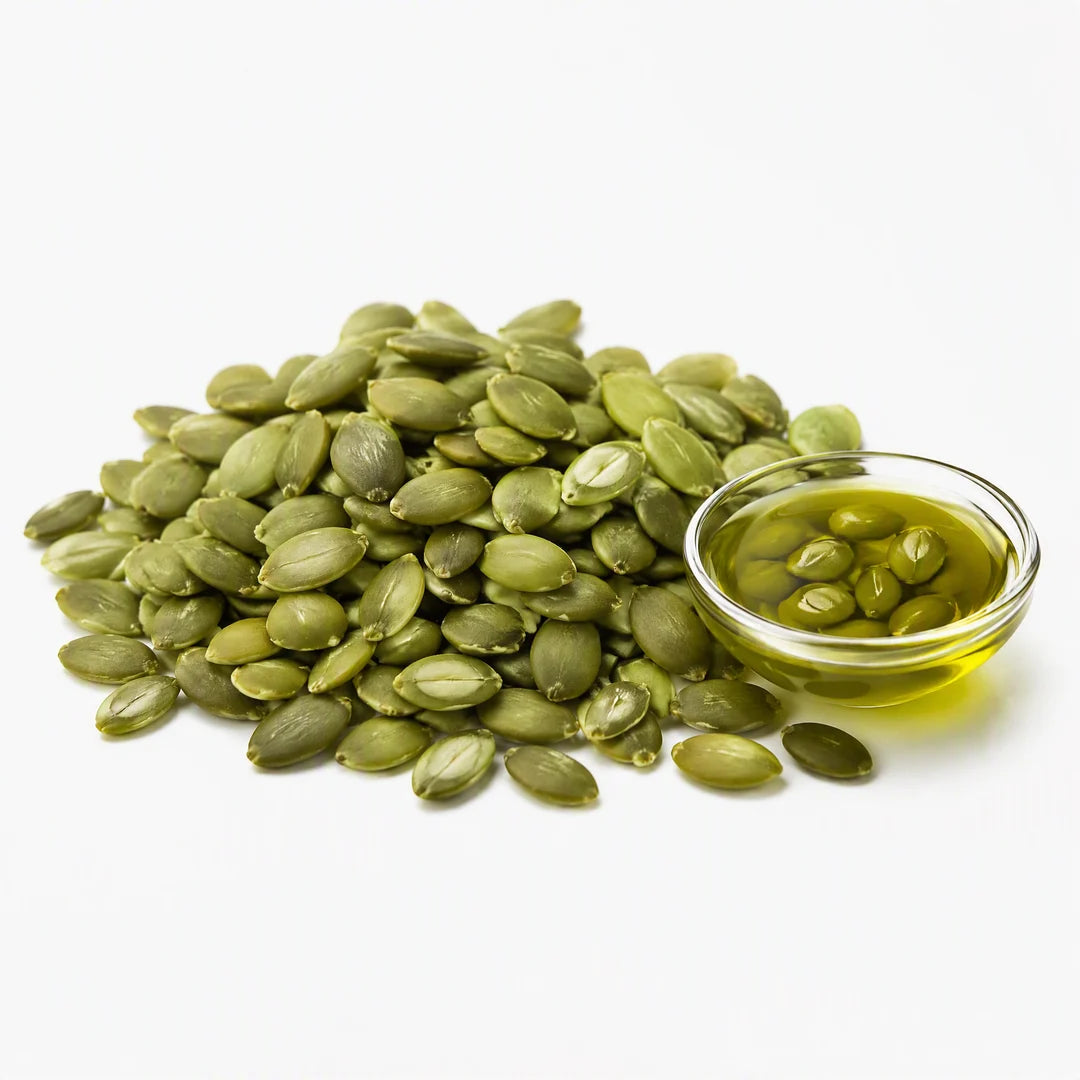 Hulled pumpkin seeds, some split open, beside a dish of cold-pressed pumpkin seed oil